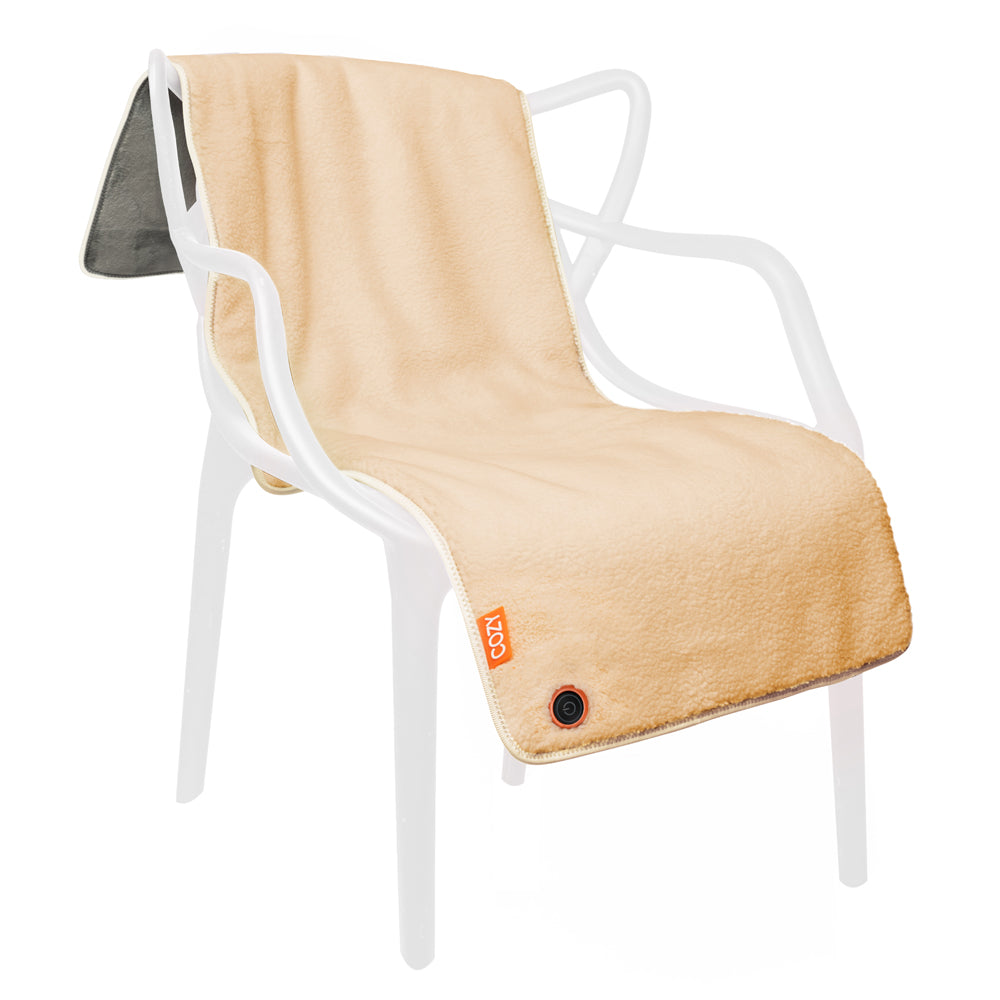 The COZY Heated Throw & Seat Cover Pad - JORV by Cozy Cushion EU, with plush beige fabric and gray underside, is draped over a modern white chair. It features a control button and eco-friendly heating for cozy comfort.