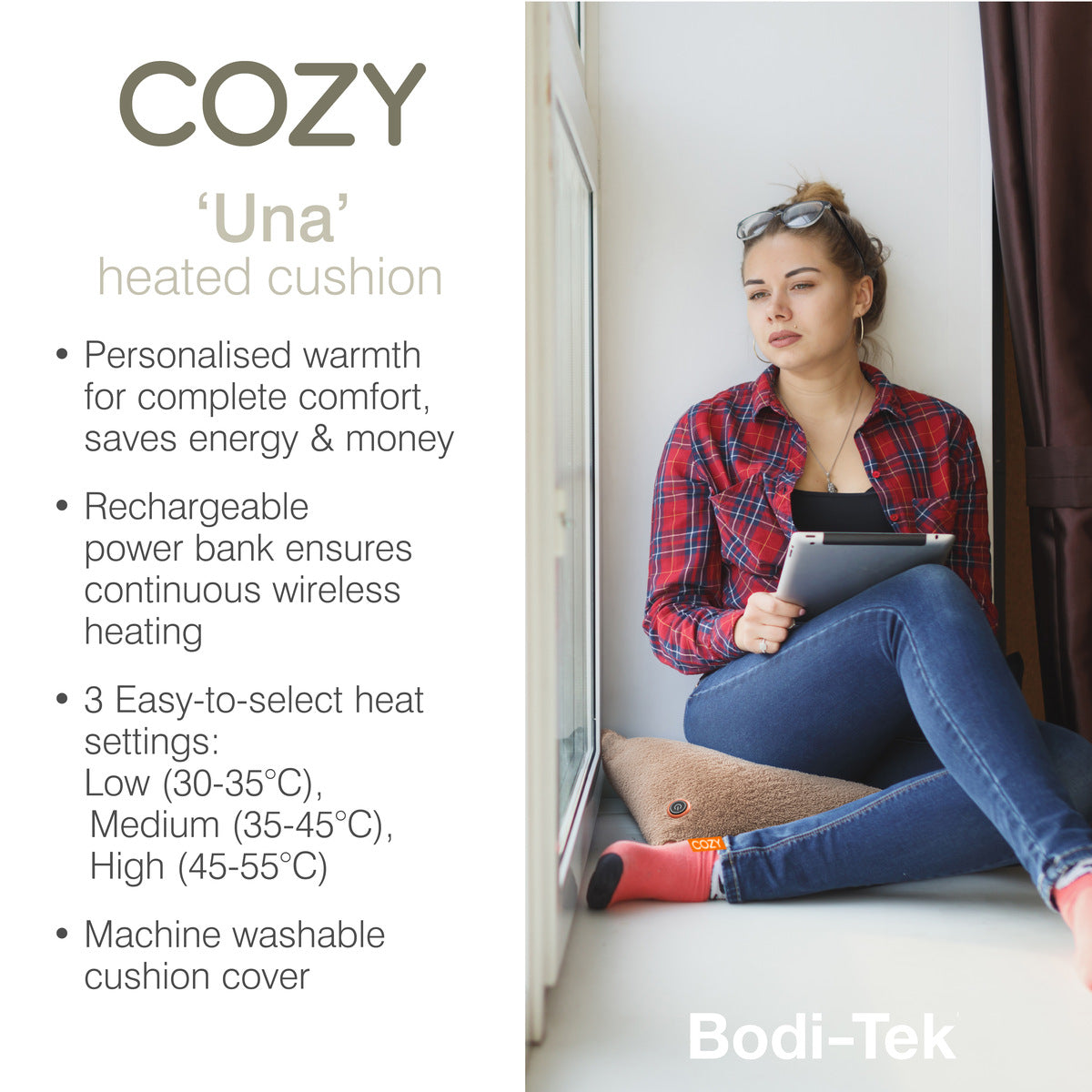 A woman sits by a window using a tablet on the COZY Heated Cushion Cordless - UNA Woolly (45cm x 45cm) from Cozy Cushion EU, featuring adjustable heat, a rechargeable battery, and a washable cover.