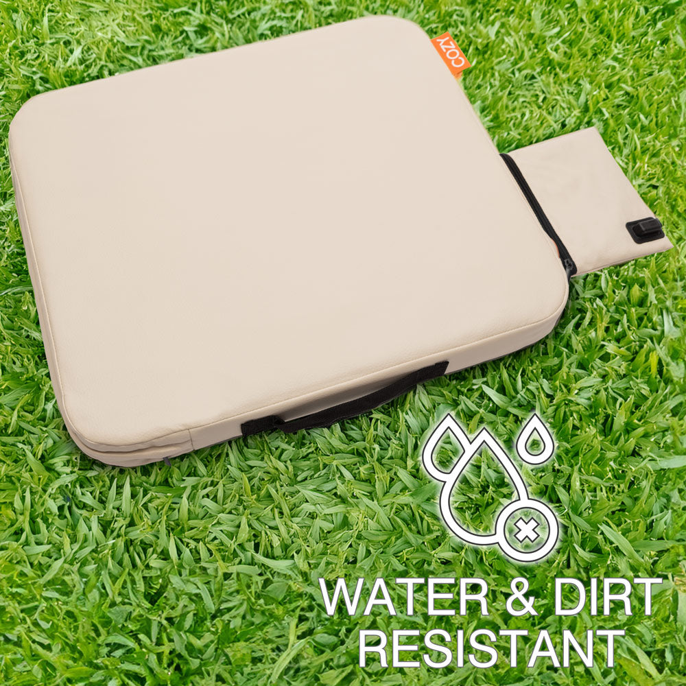 The COZY Cordless Heated Seat Pad - JORD by Cozy Cushion EU, a beige rectangular cushion with a black handle and pull-out flap, sits on green grass. Overlay text and icons highlight its portable, water- and dirt-resistant design.