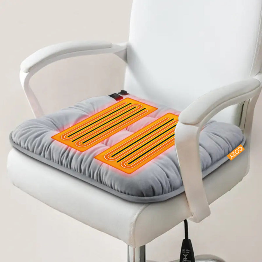 The COZY Heated Seat Cushion - LUKSU by Cozy Cushion EU is a soft, square, light gray seat pad with plush filling and an orange COZY tag. It features a quilted design and can be powered by a rechargeable power bank for added warmth.