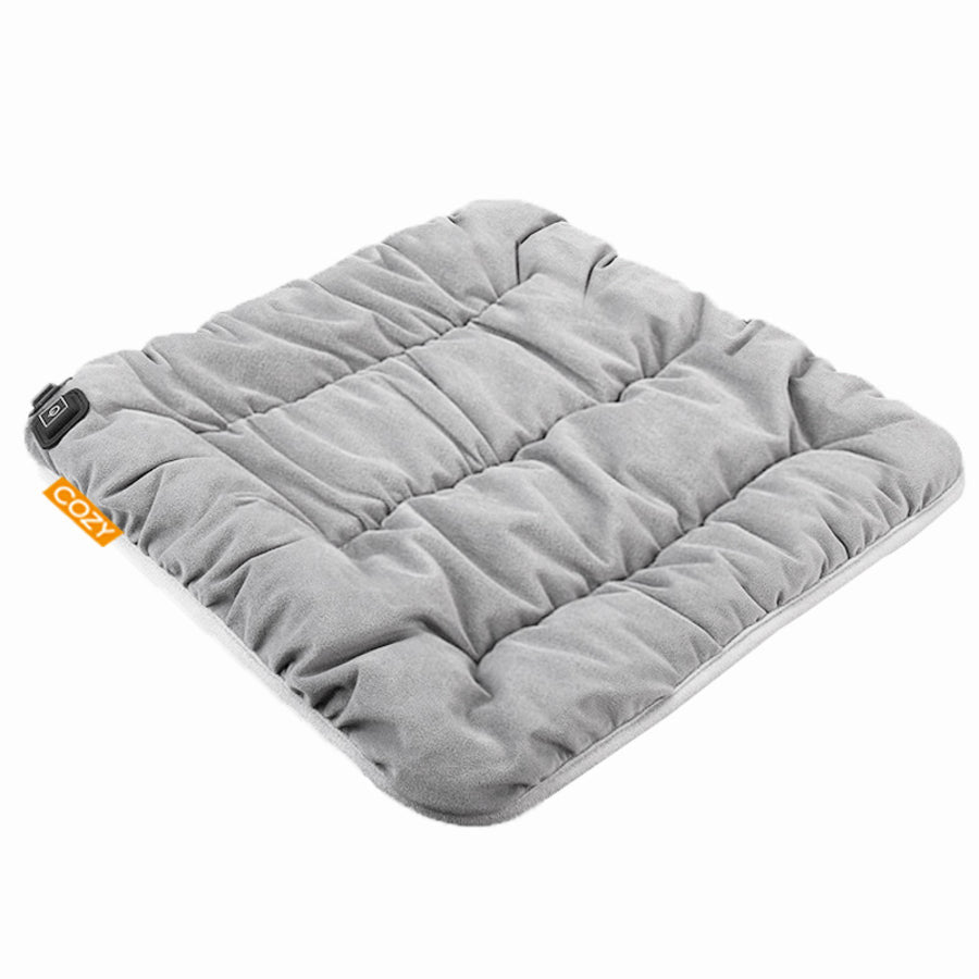 The COZY Heated Seat Cushion - LUKSU by Cozy Cushion EU is a soft, square, light gray seat pad with plush filling and an orange COZY tag. It features a quilted design and can be powered by a rechargeable power bank for added warmth.