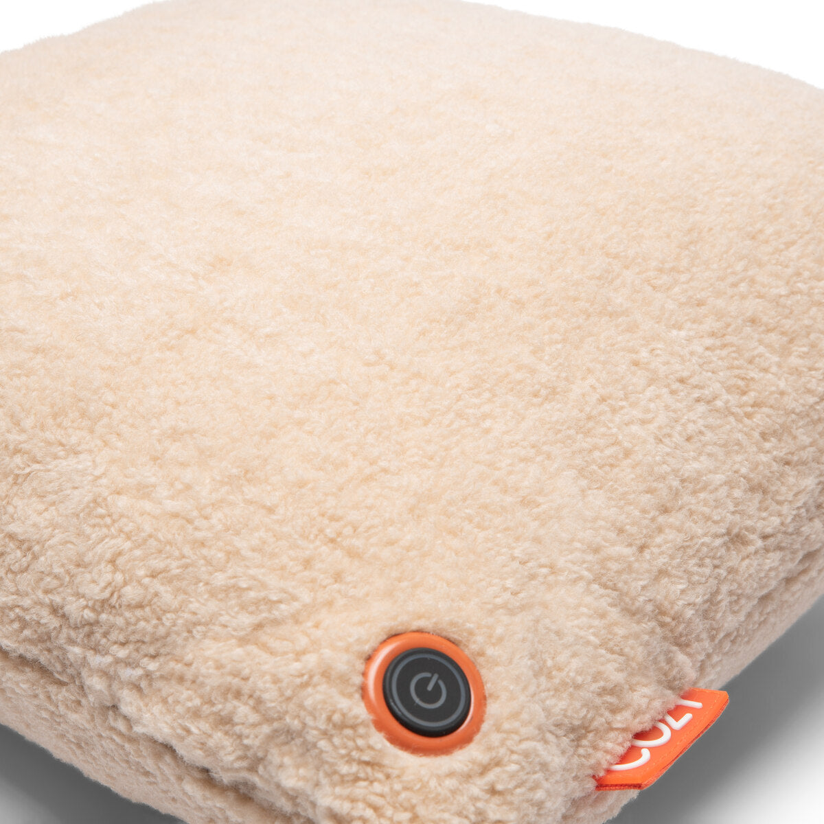 A close-up of the COZY Heated Cushion Cordless - UNA Woolly (45cm x 45cm) by Cozy Cushion EU shows its soft beige fabric and orange power button, revealing it as a rechargeable, cordless heated cushion.